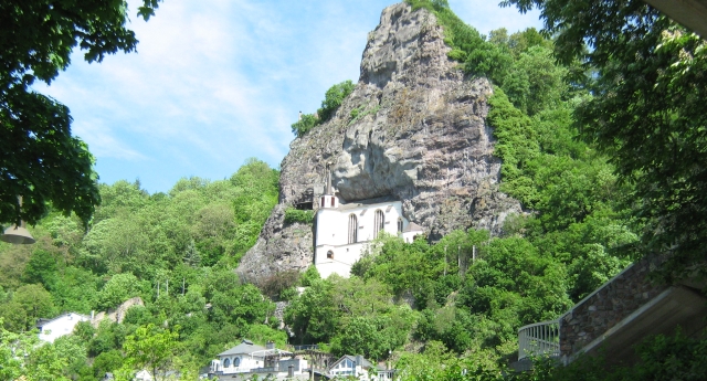 a vertical rock face amongst trees with a white church built deep into the rock